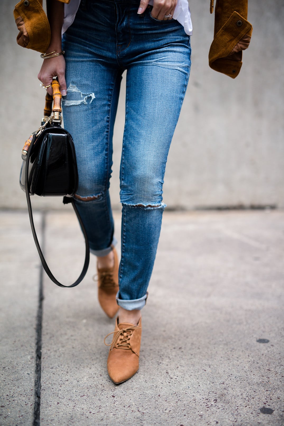 Pam Hetlinger wearing a tan faux suede jacket, nina shoes booties, madewell jeans, white button front shirt, gucci bamboo top handle handbag, free people lace crop top and mirrored aviators