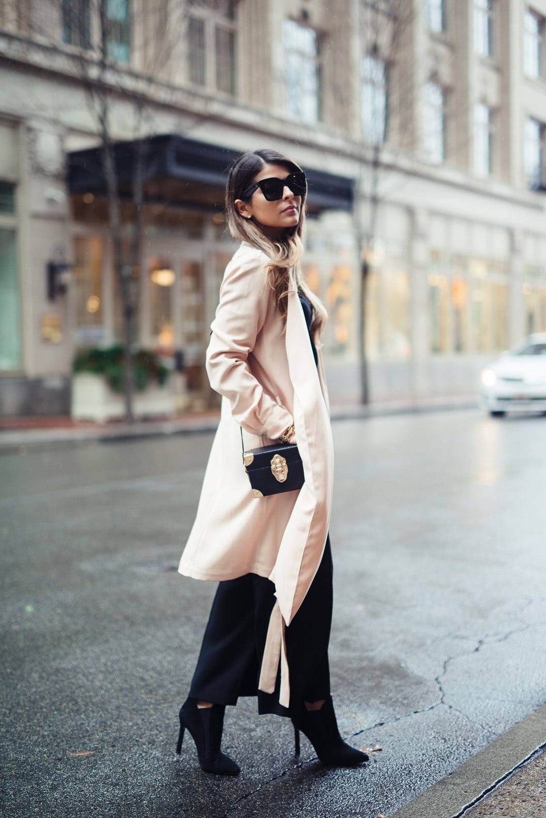 Pam Hetlinger wearing a cold shoulder sweater, black culottes, black booties, and a camel trench coat. Valentine's day outfit idea.