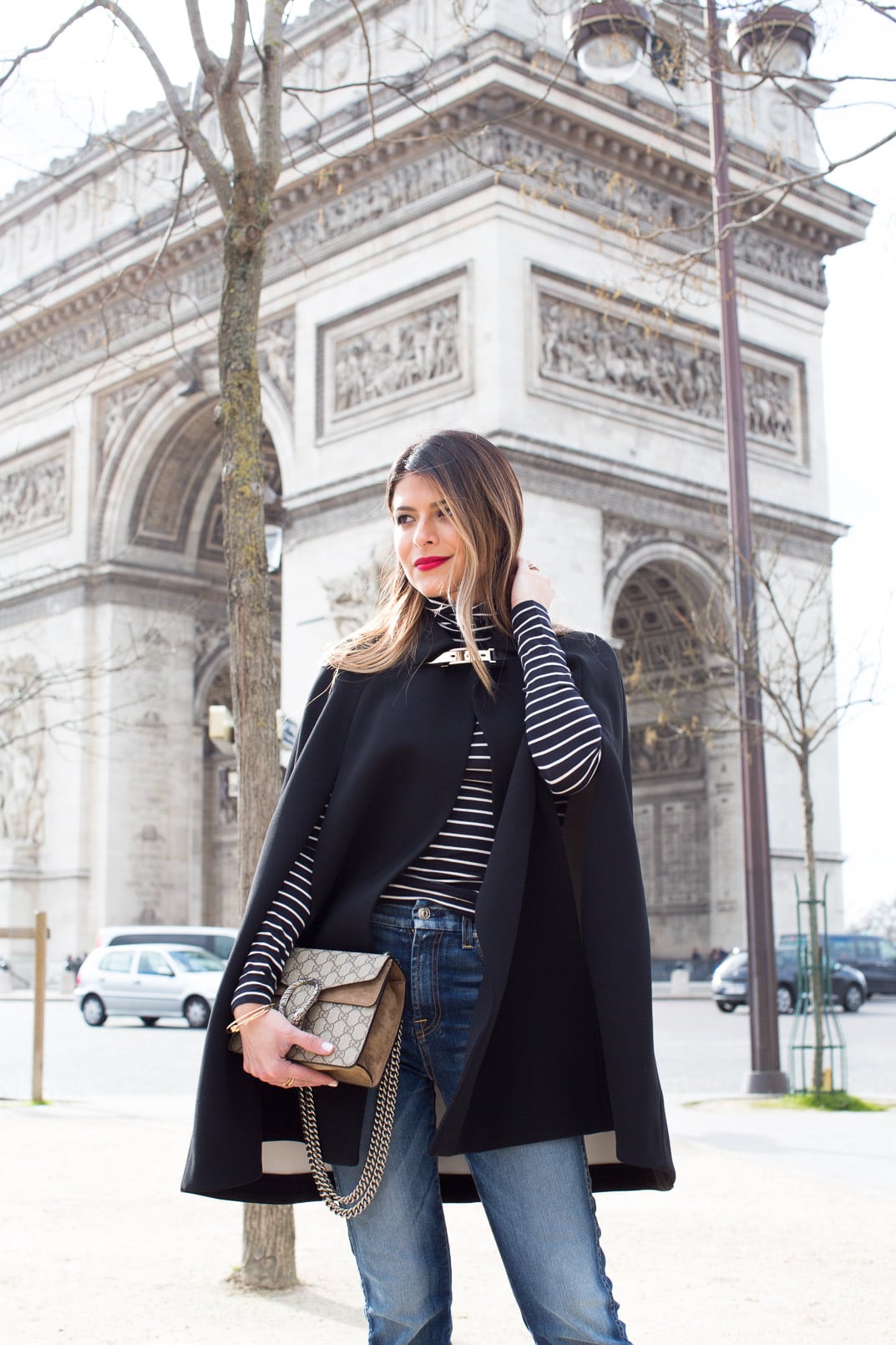 Pam Hetlinger wearing a Kate Spade Jenji Capelet, striped turtleneck, 7 for all Mankind skinny cropped jeans, Gucci Dionysus GG Supreme shoulder bag and balenciage buckle booties. Paris Fashion Week.