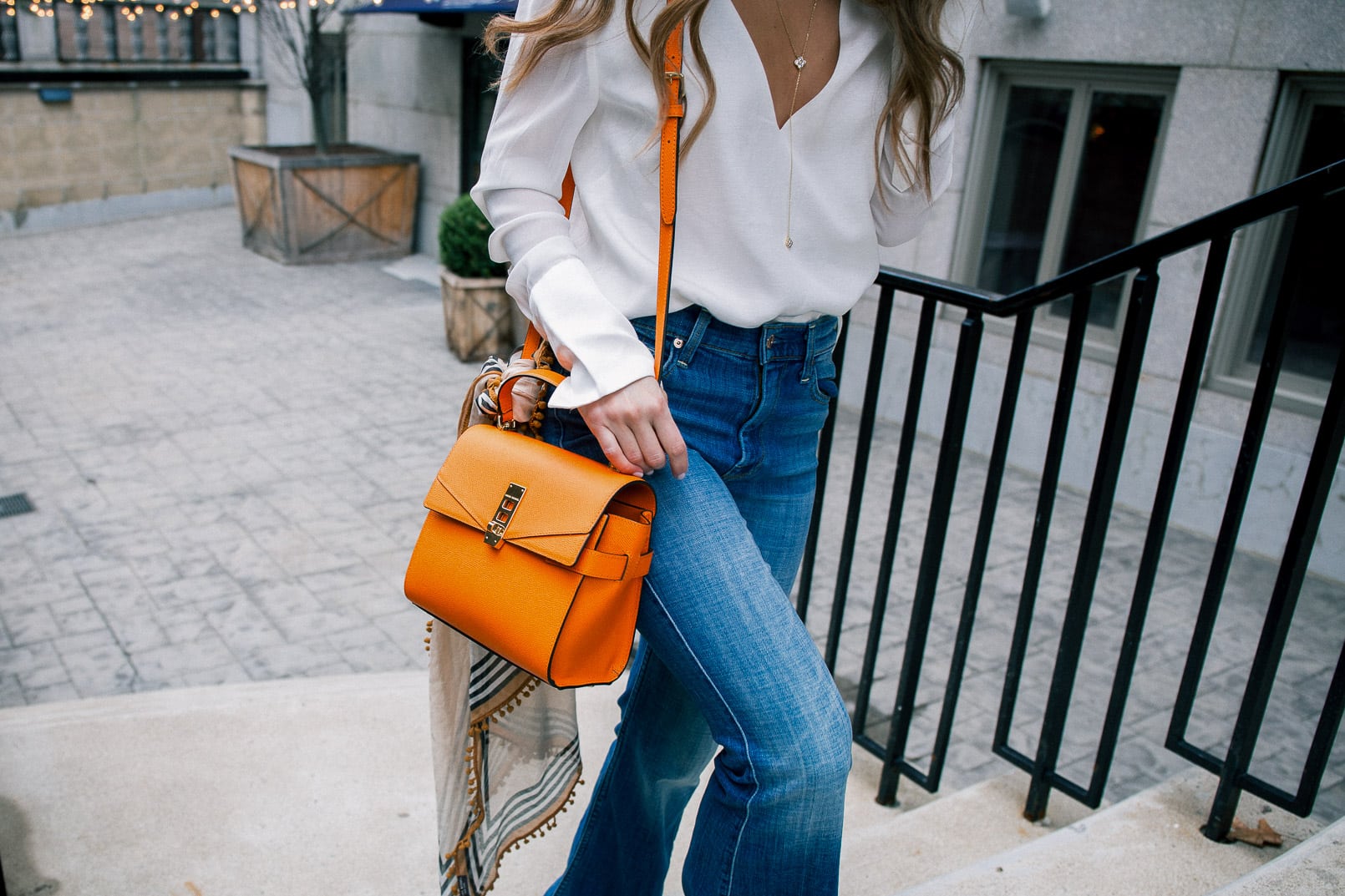 Pam Hetlinger wearing a henri bendel UPTOWN SATCHEL, 7 for all mankind flares, white v neck top, and red lipstick, colorful bag for spring.