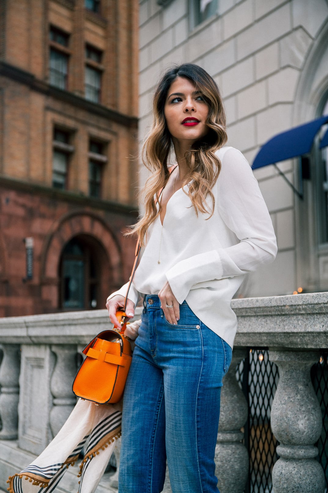 Pam Hetlinger wearing a henri bendel UPTOWN SATCHEL, 7 for all mankind flares, white v neck top, and red lipstick, colorful bag for spring.