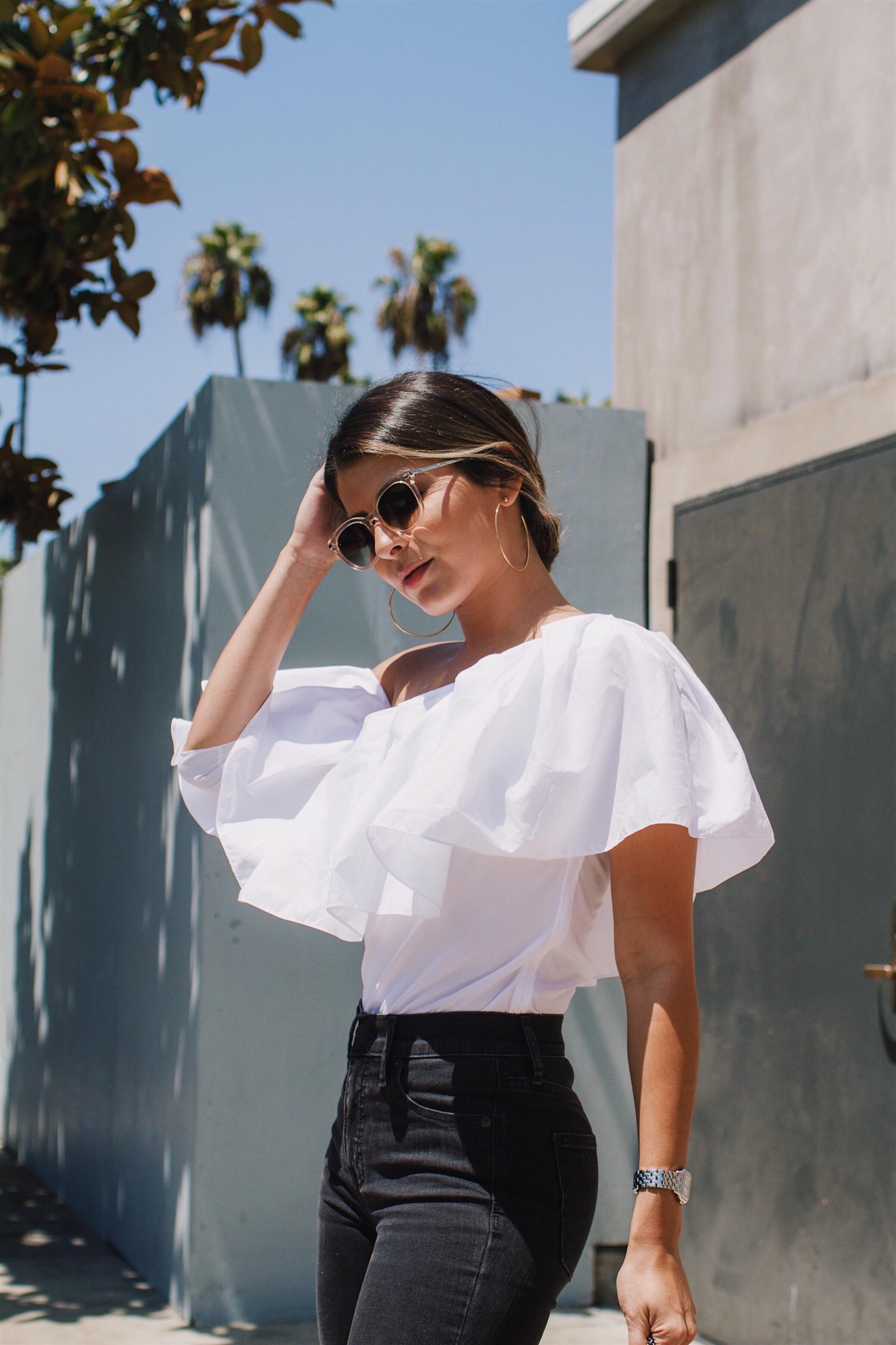 Pam Hetlinger wearing a White Ruffle Top styled with black ripped jeans and velvet pumps.