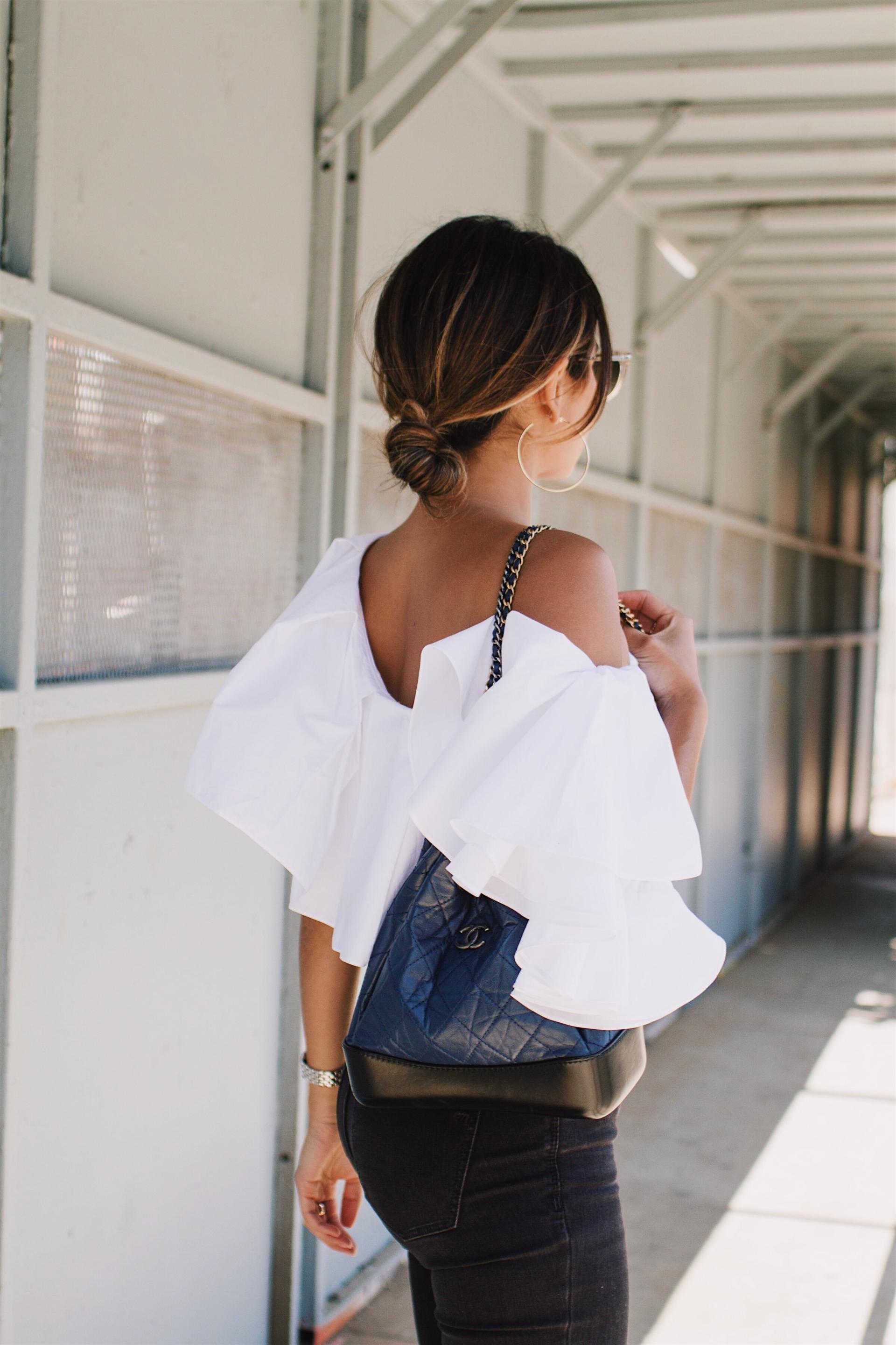 Pam Hetlinger wearing a White Ruffle Top styled with black ripped jeans and velvet pumps.