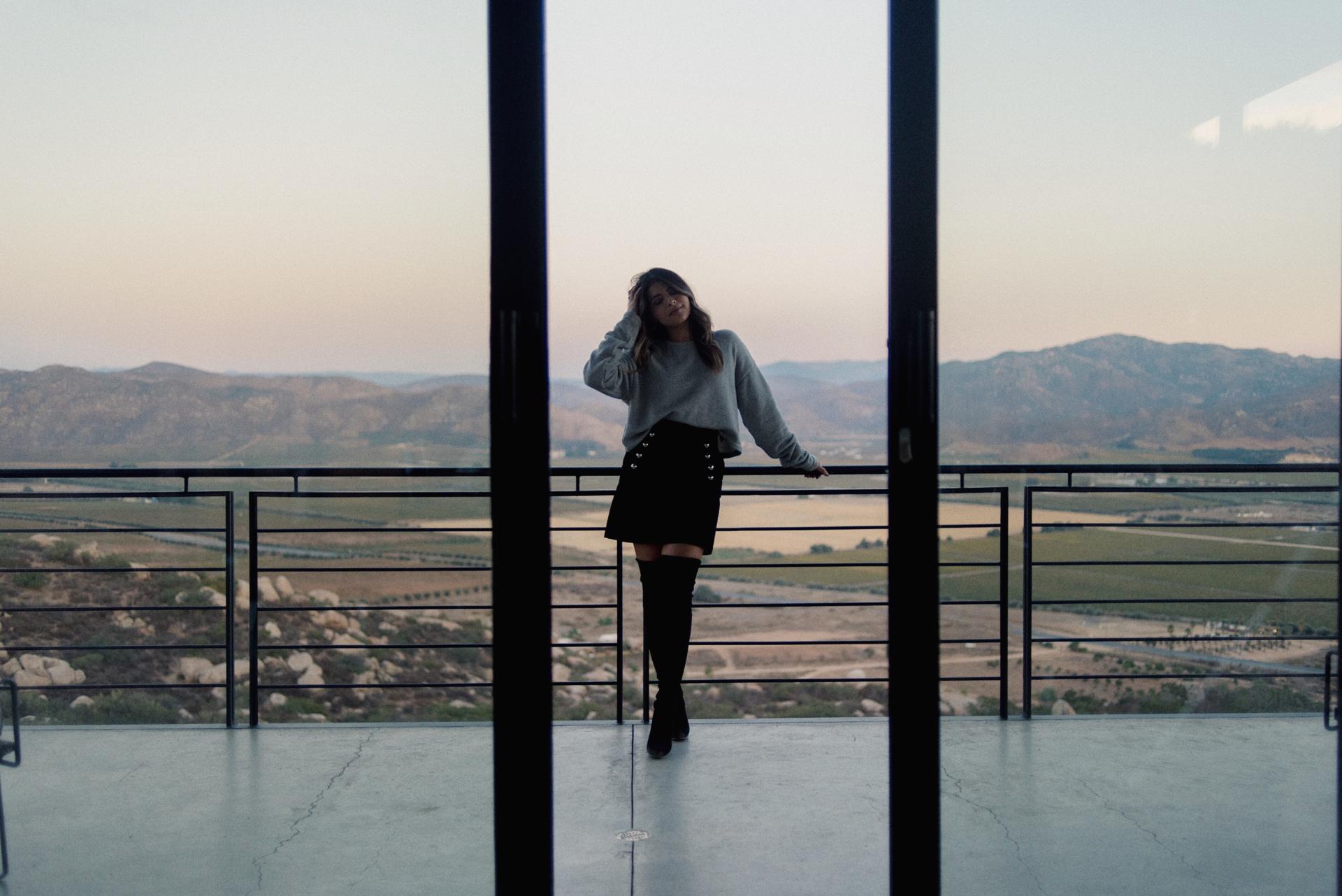 Pam Hetlinger wearing a grey sweater, black skirt and over the knee boots during a sunset in Valle de Guadalupe