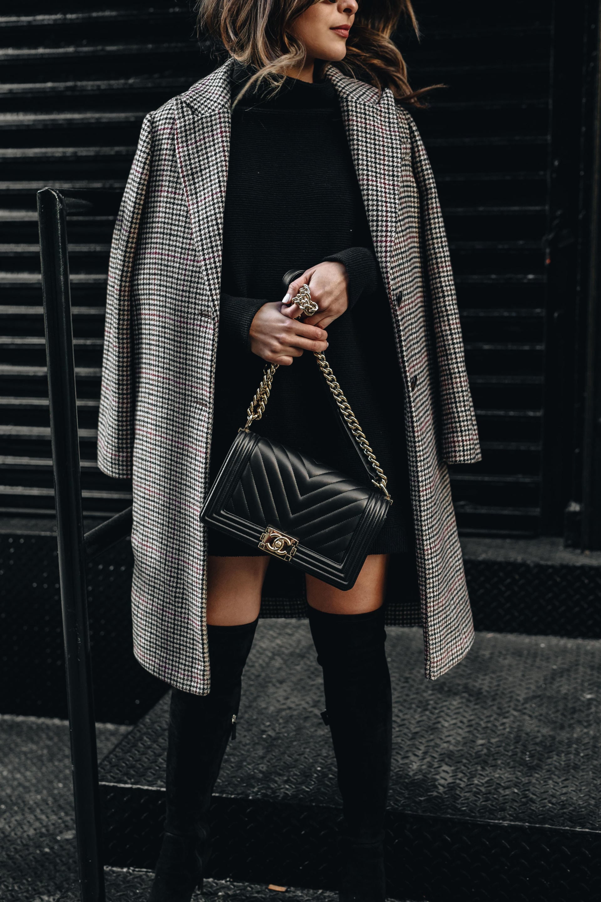 Pam Hetlinger of The Girl From Panama shows how to style over the knee boots in a chic way with a plaid blazer and black sweater dress